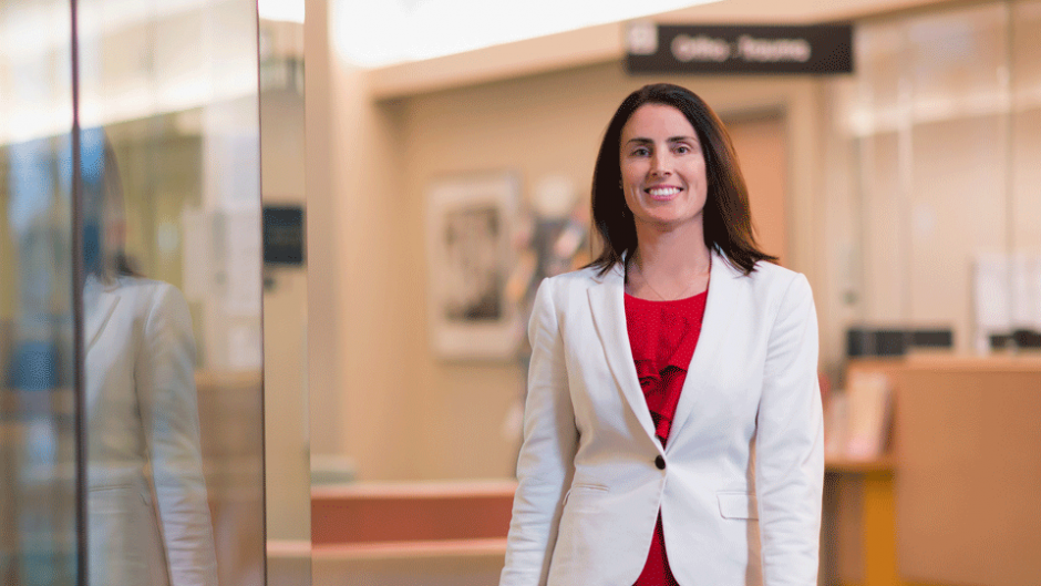 Dr. Tara Sedlak, wearing a red dress and white blazer, walks through a waiting area