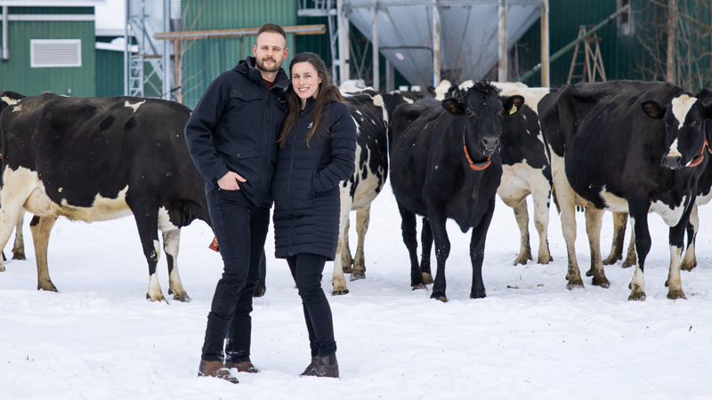 Dr. Jenn Vandenberg and her husband Dan standing in snow in front of cows and farm buildings