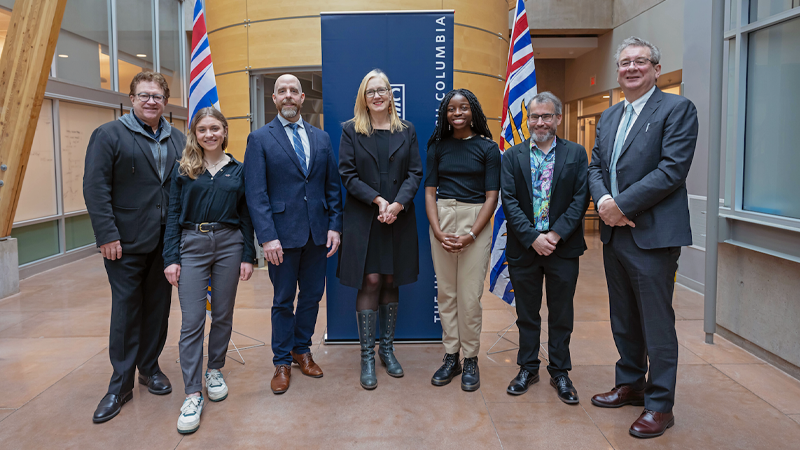 Speakers at the announcement event, including UBC leadership and Minister Brenda Bailey, pose as a group in front of the B.C. flag and a UBC banner